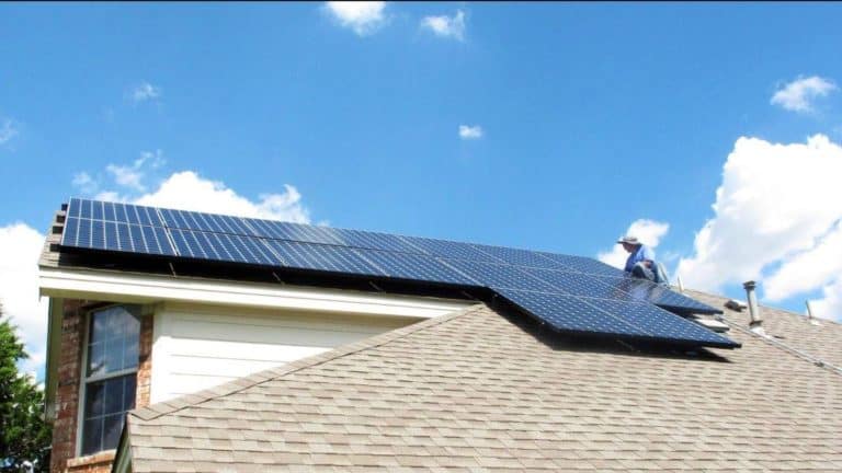 Roof view of solar panels installed on roof of house with a man working on it under bright blue sky