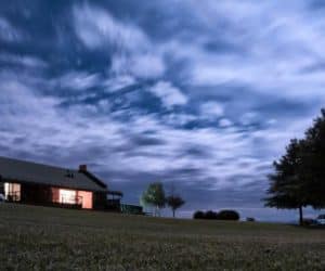 Illuminated house and garden under cloudy sky