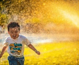 Boy running having fun while sprinkler releases water