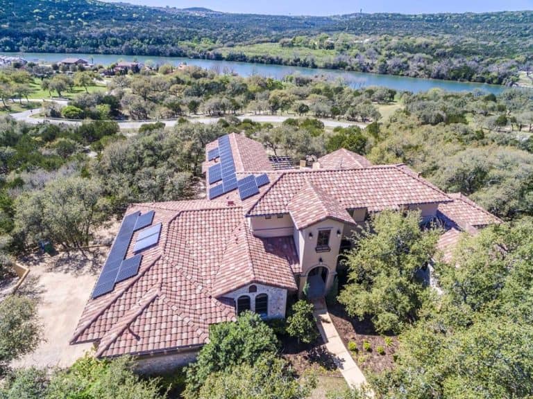 View of house roof in Austin, Texas with solar panels, green areas and lake behind