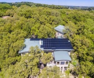 front view of house roof with installed solar panels and surrounded by trees in West Lake Hills, Texas