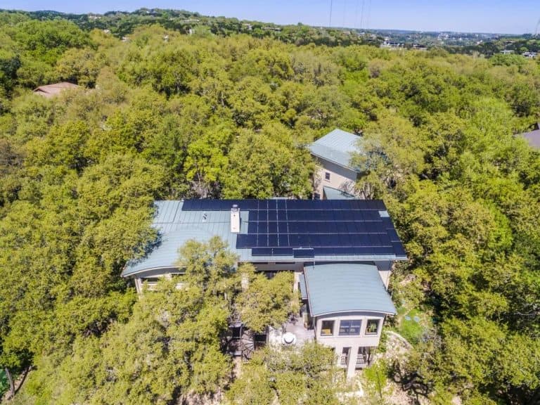 front view of house roof with installed solar panels and surrounded by trees in West Lake Hills, Texas