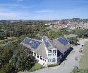 Front aerial view of white building with solar panels on the roof and surrounded by trees