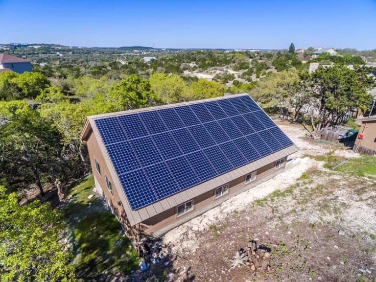 Lateral view of house roof in Great Divide, Bee Cave, Texas with solar panels installed and green areas behind