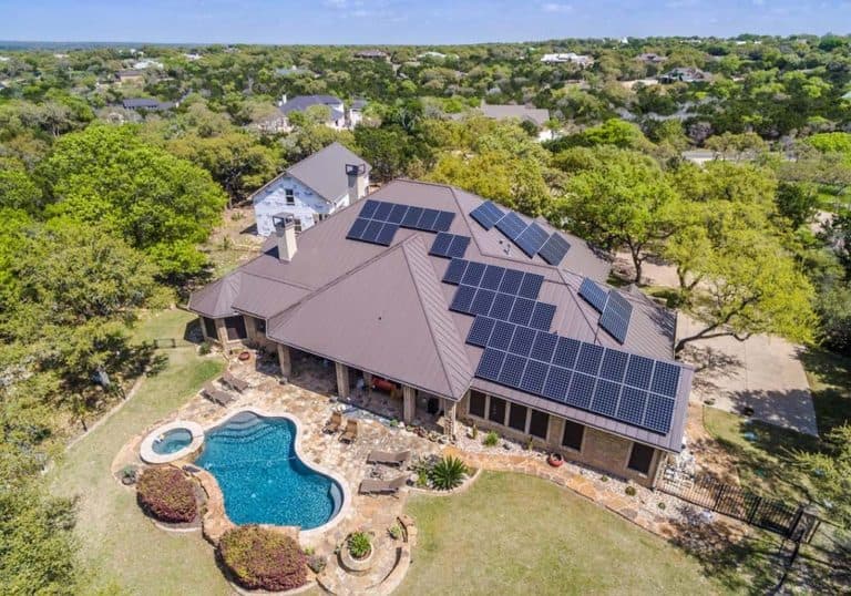 Aerial view of backyard of house with solar panels installed on roof and trees around in Austin, Texas