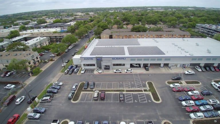 Front view of Austin Subaru dealership in Austin, Texas with array of solar panels on roof and parking lot