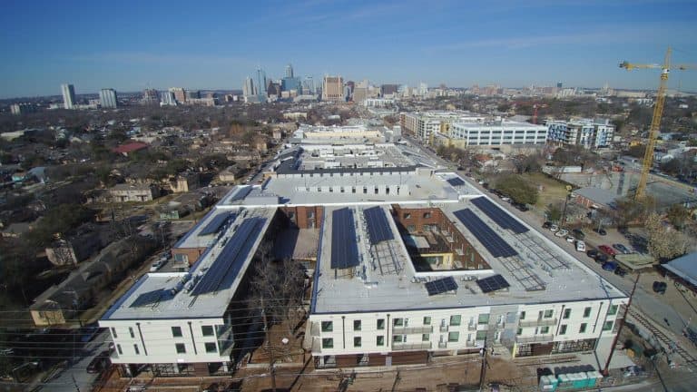 Back view of white building with solar panels on the roof and businesses around