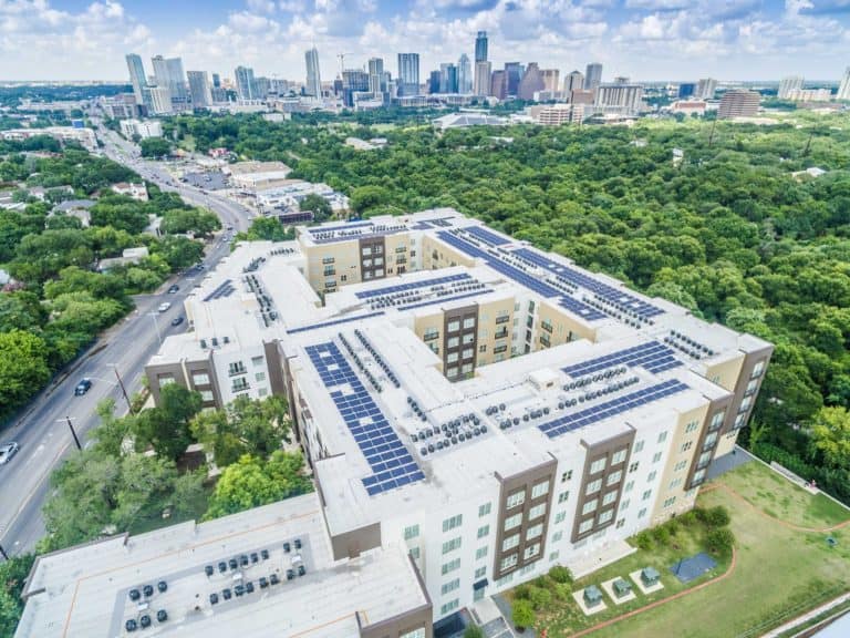 Side aerial view of apartment buildings Hanover South Lamar in Austin, Texas with solar panels on the roof and downtown view