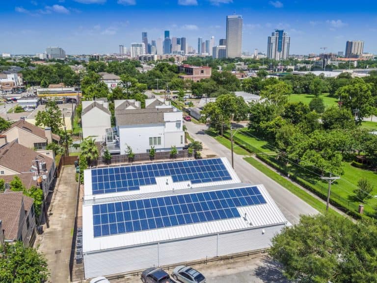 Drone back view of solar panels installed on roof of commercial building and downtown view behind