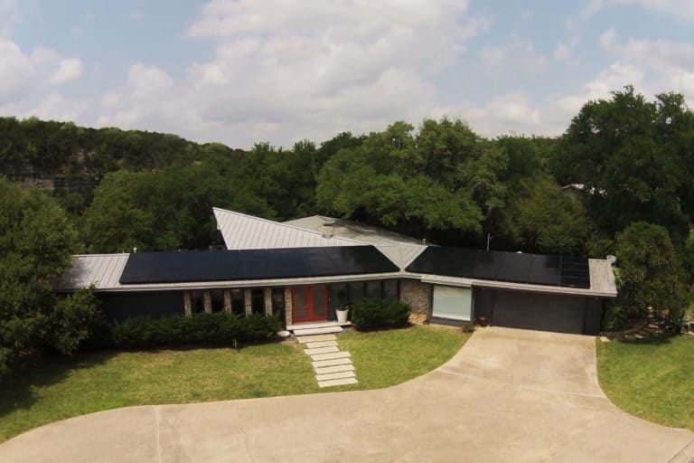House in Lakemoore Drive, Northwest Hills, Texas with solar panels installed on the roof and trees behind