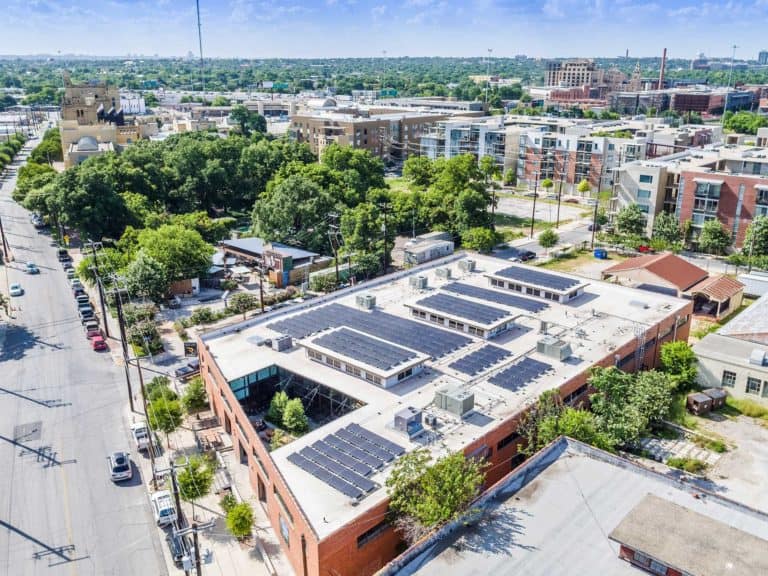 Drone side view of Overland Partner's building with solar panels installed on the roof, residential neighborhood in the back under blue sky