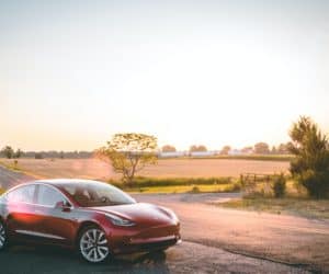 Electric vehicle made by Tesla parked on the side of a road with a field in the background