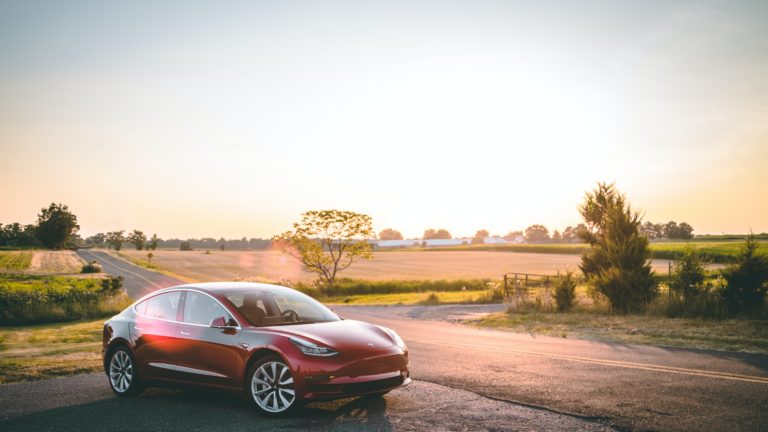Electric vehicle made by Tesla parked on the side of a road with a field in the background