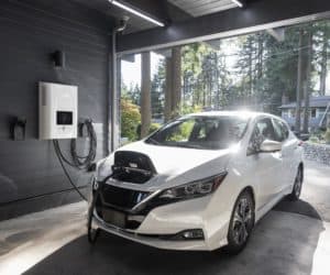 A white electric vehicle parked in a residential garage with the battery connected to a home charging port.