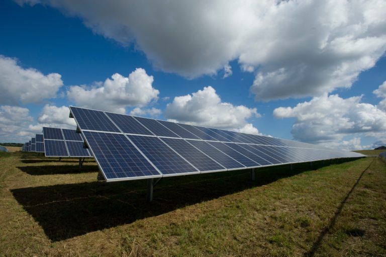 Solar panel array in a countryside field under a blue sky with scattered clouds.