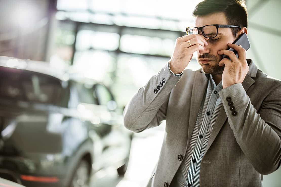 Man with glasses looking worried talking on the phone and holding his nose