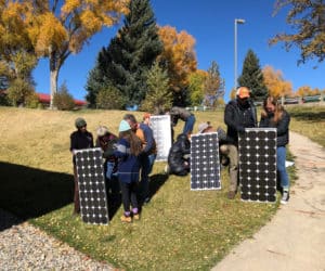 Team members of the Equitable Solar Solutions' program holding several solar panels in the grass