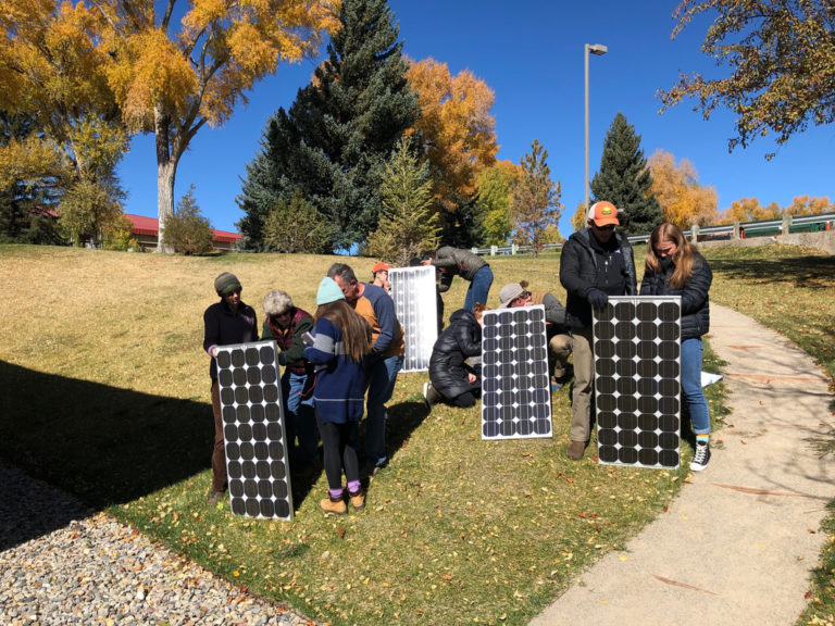 Team members of the Equitable Solar Solutions' program holding several solar panels in the grass