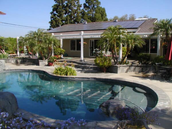 pool infront of home with solar panels on roof and palm trees surrounding porch