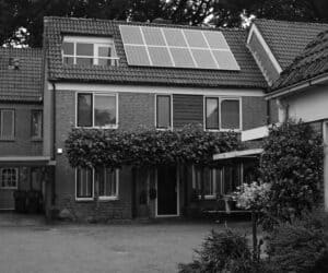 Black and white photo of a house with one solar panel array attached to its roof.