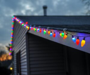A zoomed-in photo of colorful christmas lights mounted on the edge of a home's roof.