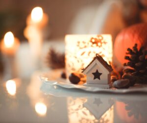 Holiday-themed photo with lit candles, pine cones and holiday decor on a tabletop.