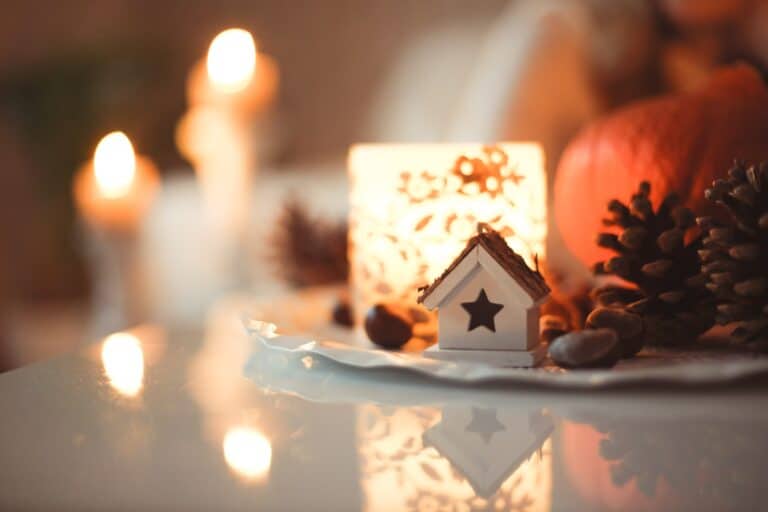Holiday-themed photo with lit candles, pine cones and holiday decor on a tabletop.