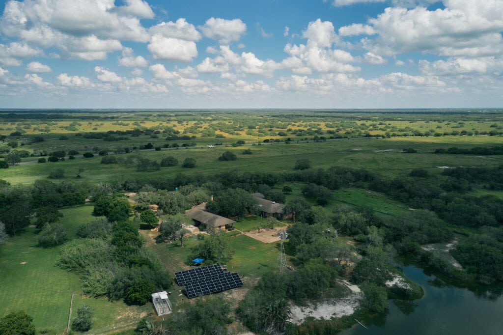 high aerial view of ranch house, ground mount solar panels, and the green coastal grasslands of Texas