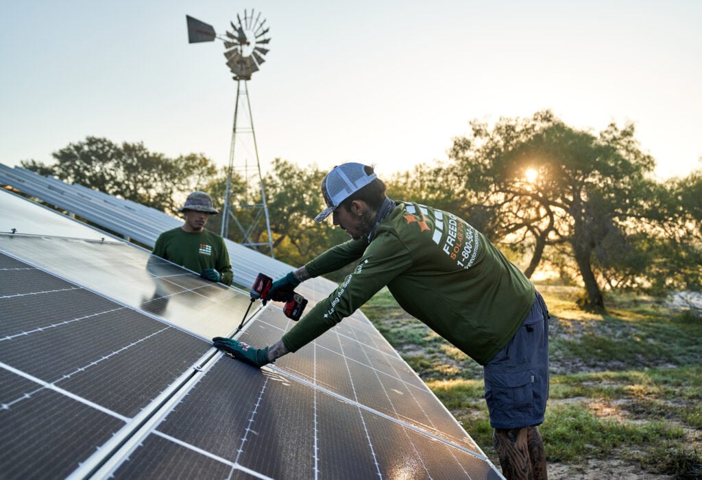 worker drilling solar panel to ground mount during sunset