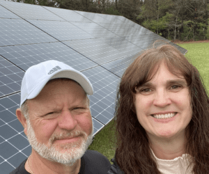 Couple standing in front of solar panel installed on the ground