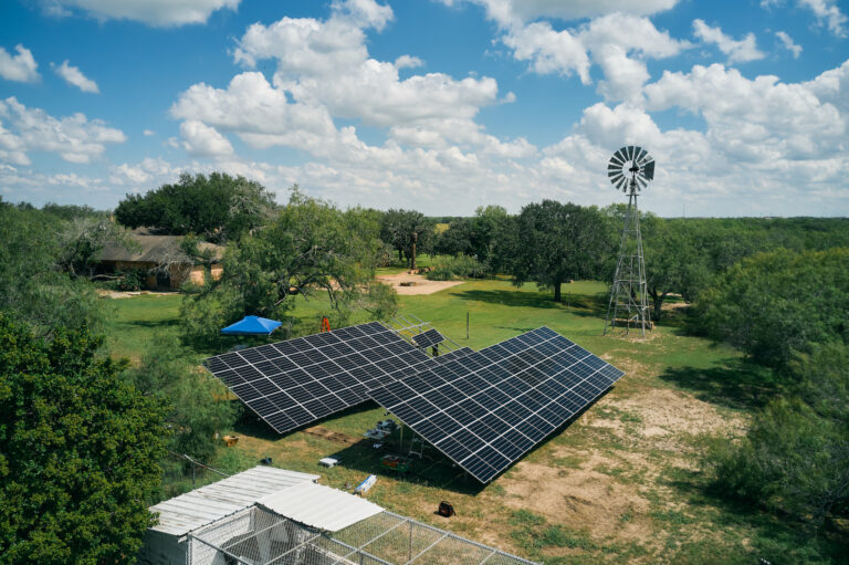 Installation of solar panels on the ground in Texas, with a small windmill behind