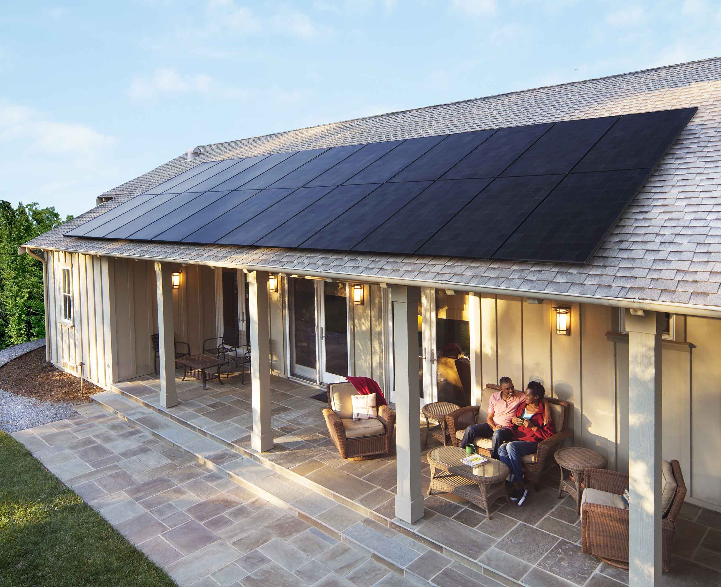 Couple sitting on porch of house with solar panels on roof
