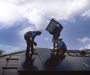 Three energy technicians installing solar panels on a roof