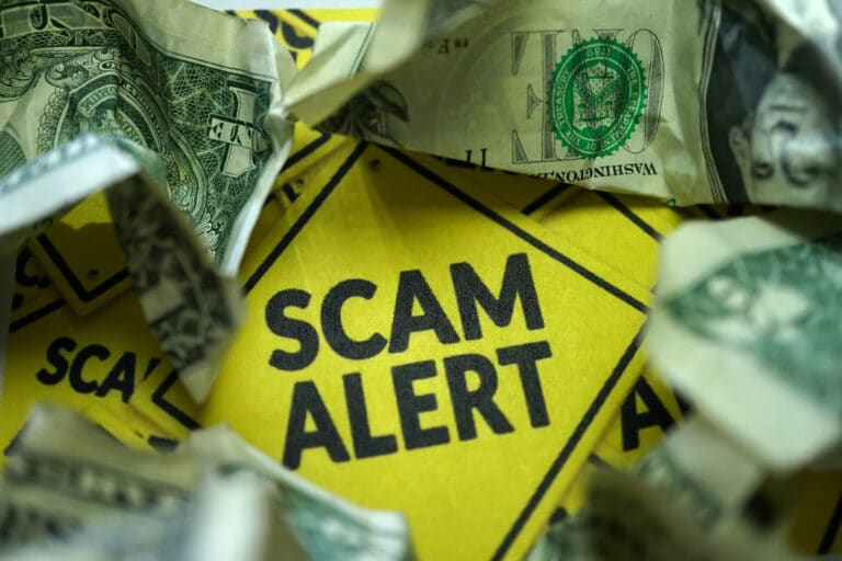 Yellow sign that says "scam alert" with scrunched dollar bill surrounding it.