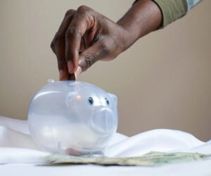 Close up image of a hand putting a coin into a piggy bank
