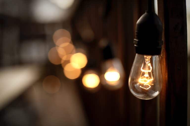 Close up of a lit up lightbulb in a dark room with blurred bulb lights behind it at a distance