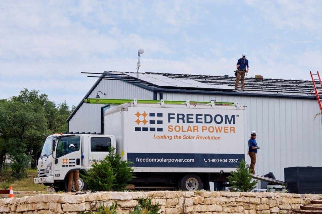 Distant shot of a Freedom Solar branded vehicle with a crew working on Todd White's art studio